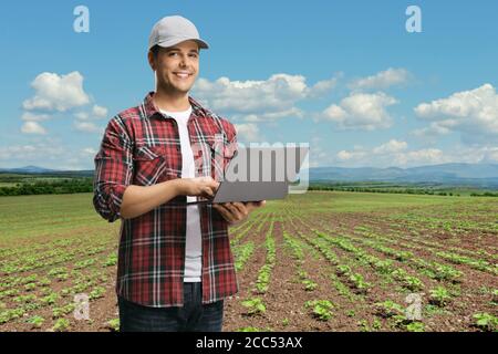 Junger Mann in einem karierten Hemd mit einem Laptop Und die Kamera auf einem Feld mit Pflanzen betrachten Stockfoto