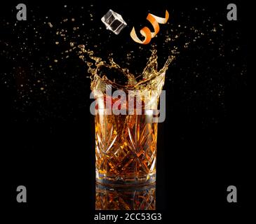 Orangenschale und Eis fallen in spritzendem Cocktail isoliert auf Schwarz Stockfoto