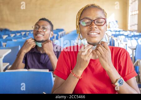 Junge afrikanische Studenten in einem Klassenzimmer nehmen ihre medizinischen Masken Aus Stockfoto