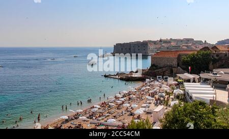 Ein überfüllter Touristenstrand in Dubrovnik im Sommer, mit der Altstadt im Hintergrund, Kroatien Stockfoto