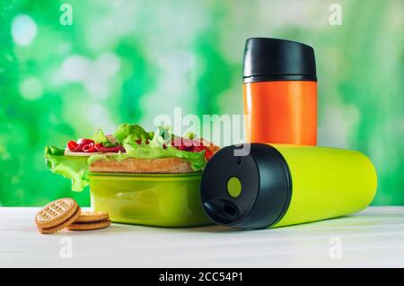 Farbe Thermoskanne Tassen neben Lunchbox auf weißem Tisch Stockfoto