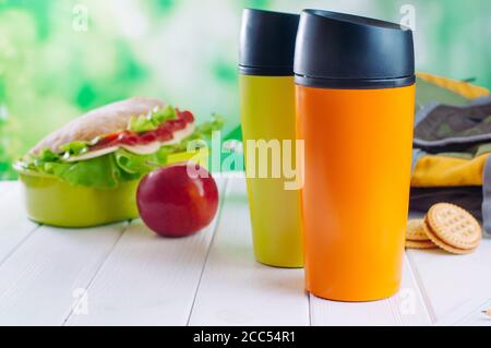 Farbe Thermoskanne Tassen neben Lunchbox und Rucksack auf dem Tisch Stockfoto