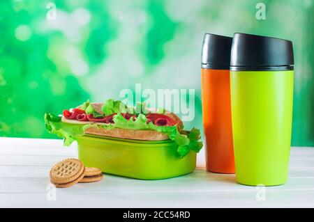 Farbe Thermoskanne Tassen neben Lunchbox auf dem weißen Holz Tabelle Stockfoto