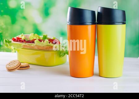 Farbe Thermoskanne Tassen neben Lunchbox auf dem weißen Holz Hintergrund Stockfoto