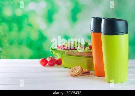 Farbe Thermoskannen Becher in der Nähe von Lunchbox auf weißem Holzhintergrund Stockfoto