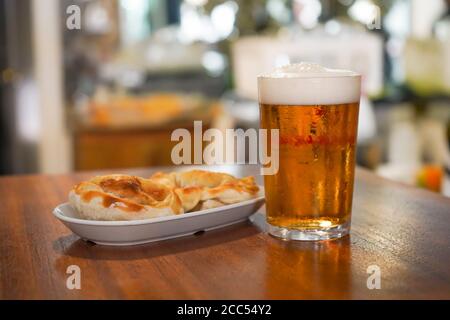 Zwei Empanadas serviert als Tapas mit einem Glas Bier daneben. Stockfoto