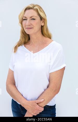 Studio Porträt einer attraktiven mittleren Alters blonde Frau lächelnd Auf weißem Hintergrund mit einem weißen T-Shirt und blau Jeans Stockfoto