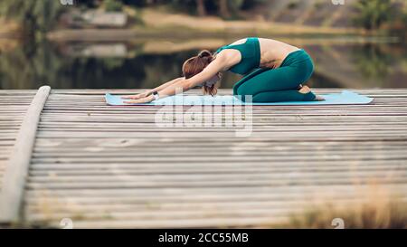Sportlerin macht Yoga auf hölzerner Plattform Stockfoto