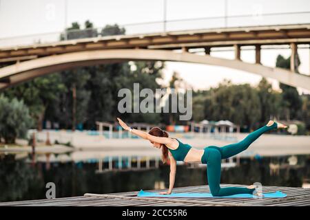 Sportlerin macht Yoga auf hölzerner Plattform Stockfoto
