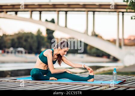 Sportlerin macht Yoga auf hölzerner Plattform Stockfoto