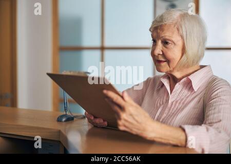 Ältere Frau trägt rosa Hemd halten Zwischenablage in der Hand Stockfoto