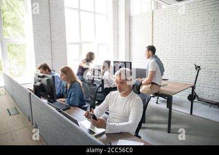 Mann, Der Am Schreibtisch Im Vielbeschäftigten Kreativbüro Arbeitet. Stockfoto