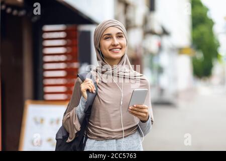 Glückliche muslimische Frau, die auf der Straße läuft und Musik hört Stockfoto