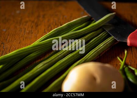 Drumstick Gemüse mit Kartoffel und Messer auf braunem Tisch Stockfoto