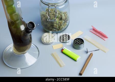 Rauchen von Cannabis Zubehör und Sachen auf grauem Hintergrund. Bong, stumpfes und gemeinsames Papier, Mahlwerk und Marihuanaknospen im Glas Stockfoto