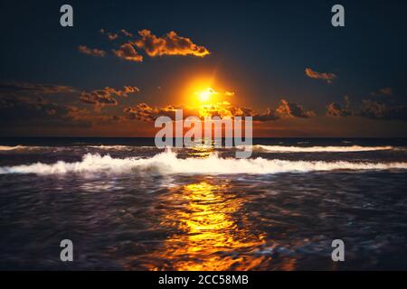 Vollmond, der über Meereswellen aufsteigt. Dramatischer Sonnenuntergang über dem Strand. Stockfoto