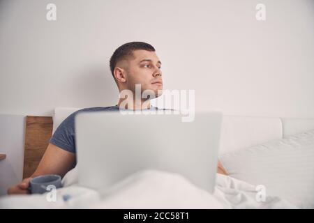 Junger Mann mit Laptop im Bett Stockfoto