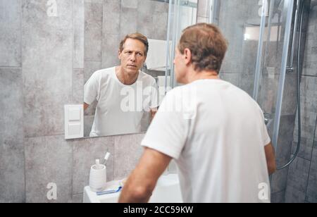 Ernsthafter Erwachsener, der in einem Badezimmer steht Stockfoto