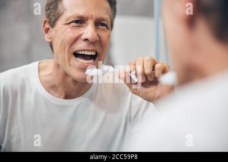 Mann mit einer Zahnbürste in der Hand, die seine Zähne untersucht Stockfoto