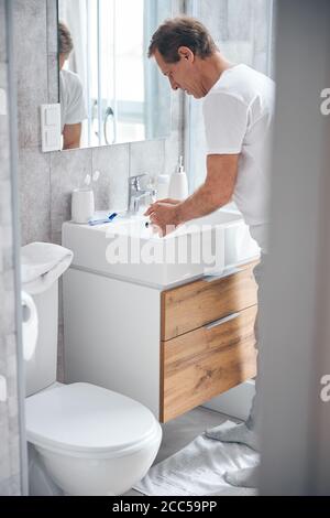 Ernsthafter Mann, der sich über das Waschbecken im Bad beugte Stockfoto