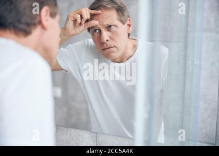 Konzentrierter Mann starrte auf seine Gesichtshaut Stockfoto