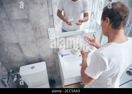 Männlich mit Nahrungsergänzungsmitteln stehen vor dem Spiegel Stockfoto