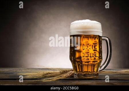 Pint blondes Bier mit Schaum auf Holztisch, mit Ähren aus Weizen. Stockfoto