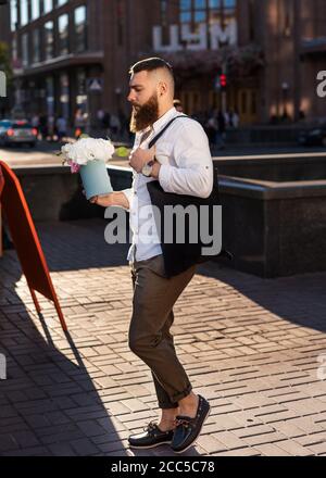 Kiew, Ukraine - 11. Juli 2020. Khreshchatyk str. gut aussehend zuversichtlich bärtigen Mann Hipster hält Geschenk Blumenkasten mit weißen Blumen auf der Straße der Stadt Stockfoto
