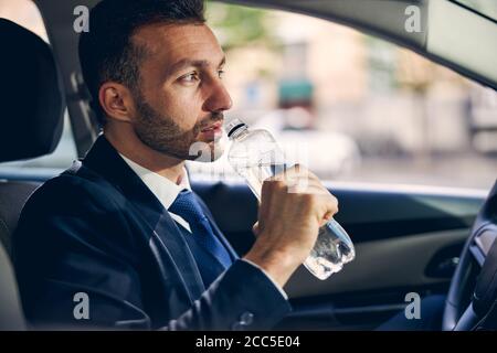 Netter junger bärtiger Mann, der Mineralwasser trinkt Stockfoto