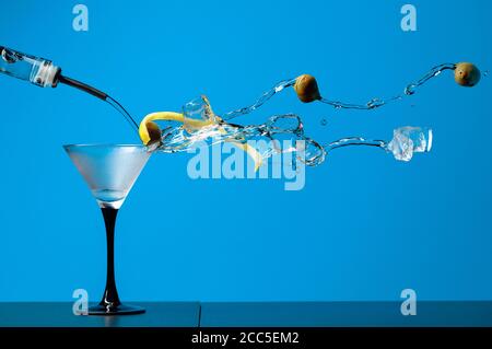 Martini mit grünen Oliven, Eis und Zitronenschale. Cocktail mit Spritzern auf blauem Hintergrund. Speicherplatz kopieren. Stockfoto