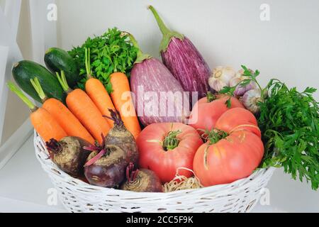 Herbstgemüse im Korb auf Regal in Holzregal in der Nähe einer weißen Wand. Vegetarisches Essen: Gurken, Tomaten, Zucchini, Petersilie und Squash. Stockfoto