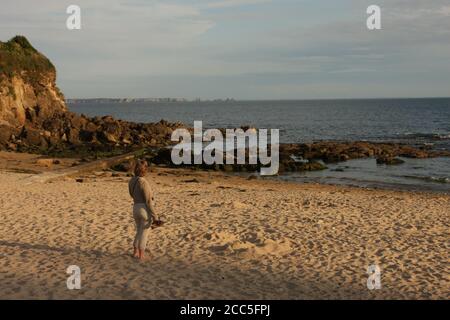 Eine Frau, die auf das Meer blickt, während sie an einem Sandstrand steht, Brixham, Devon, Großbritannien Stockfoto