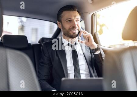 Glücklicher erfolgreicher Geschäftsmann, der im Auto telefoniert Stockfoto