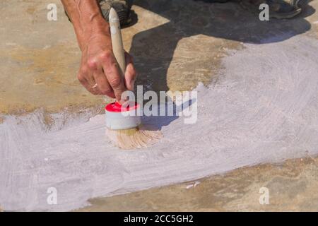 Arbeiter Hand hält eine Bürste und legt Grundierung auf Betonboden. Garten Reparaturen und Bau. Stockfoto