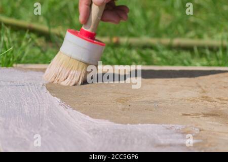 Arbeiter Hand hält eine Bürste und legt Grundierung auf Betonboden. Garten Reparaturen und Bau. Stockfoto