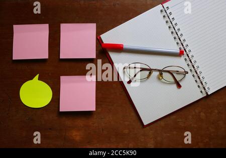 Unbeschriftete Haftnotizen neben dem offenen Notizbuch mit Stift und Brille auf Holzfläche platziert, Hochwinkelansicht Stockfoto