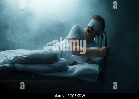 Verrückter Mann mit verbundenen Augen im Bett sitzend, psychedelisch Stockfoto