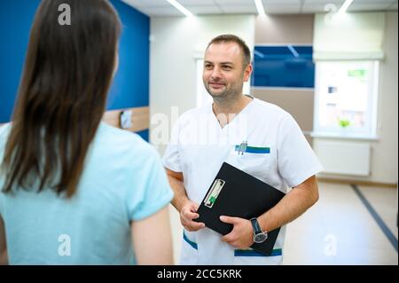 Männlicher Arzt spricht mit dem Patienten im Klinikkorridor Stockfoto