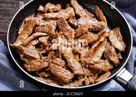 Zartes und saftiges, in Streifen geschnittenes Ribeye-Rindfleisch-Steak, Minutensteak auf einer Pfanne auf einem dunklen Holztisch, horizontale Ansicht von oben Stockfoto