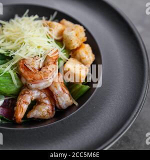 Caesar Salat mit Garnelen auf schwarzem Teller Stockfoto
