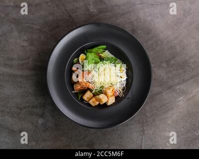 Caesar Salat mit Garnelen auf schwarzem Teller Stockfoto