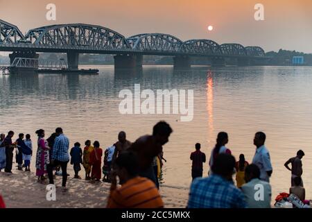 Hinduistische Pilger am Dakshineswar Ganga Ghat entlang des Hooghly Flusses mit der Vivekananda Setu Brücke im Hintergrund in Kolkata (Kalkutta), Indien. Stockfoto