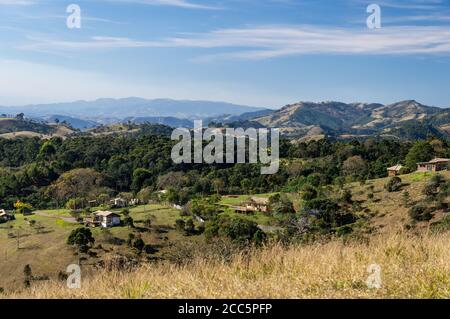 Blick von einem höheren Hügel mit Teilansicht der O Contemporario Farm unter dem späten Nachmittag wolkigen blauen Himmel mit der bergigen Cunha Landschaft auf der Rückseite. Stockfoto