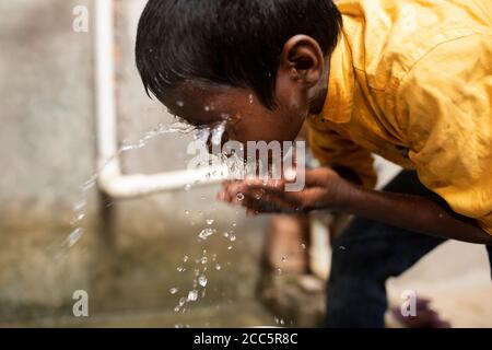 Ein Junge wäscht sein Gesicht mit Wasser aus dem neuen Wasserhahn, den seine Mutter vor kurzem im Haus der Familie in Bihar, Indien, installiert hatte. Stockfoto