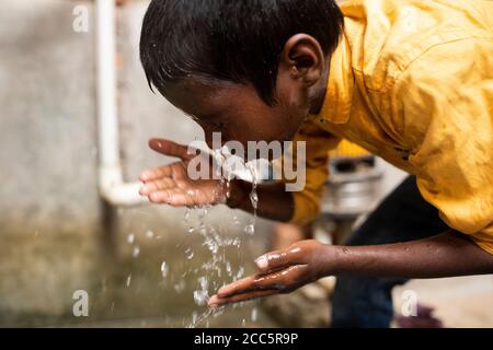 Ein Junge wäscht sein Gesicht mit Wasser aus dem neuen Wasserhahn, den seine Mutter vor kurzem im Haus der Familie in Bihar, Indien, installiert hatte. Stockfoto