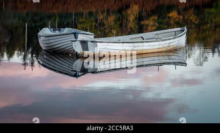 Die Spiegelungen zweier Ruderboote auf Loch Rusky A Kleines schottisches fischerloch im Trossachs National Park Stockfoto