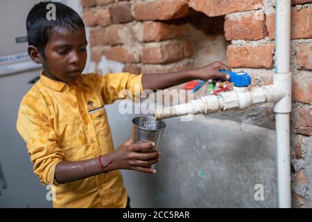 Ein achtjähriger Junge trinkt Wasser aus dem neuen Wasserhahn, den seine Mutter kürzlich im Haus der Familie in Bihar, Indien, installiert hatte. Stockfoto
