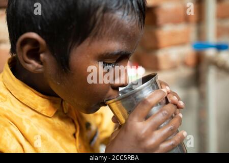 Ein achtjähriger Junge trinkt Wasser aus dem neuen Wasserhahn, den seine Mutter kürzlich im Haus der Familie in Bihar, Indien, installiert hatte. Stockfoto