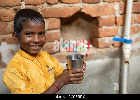 Ein achtjähriger Junge trinkt Wasser aus dem neuen Wasserhahn, den seine Mutter kürzlich im Haus der Familie in Bihar, Indien, installiert hatte. Stockfoto