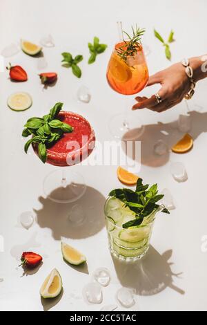 Beliebte Bar Sommer Eis alkoholische Cocktails. Gin-Tonic, Aperol Spritz und Erdbeerbasil Margarita in Gläsern und Womans Hand nach Glas rüber greifen Stockfoto